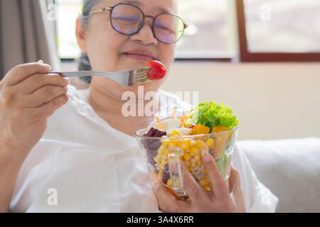 Schuss von glücklicher reifer asiatischer Seniorin, die zu Hause gesundes Essen isst. Das Konzept der gesunden Ernährung im Ruhestand. Kopierbereich, selektiver Fokus. Stockfoto