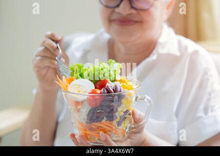 Eine ältere Frau, die bereit ist, einen Salat aus frischen und getrockneten Früchten zu essen. Frühstück oder Mittagessen, Konzept für gesunde Ernährung. Stockfoto