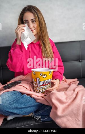 Traurige Frau, die Tränen mit einem Taschentuch abwischt, während sie zu Hause einen Film oder eine fernsehsendung ansieht Stockfoto