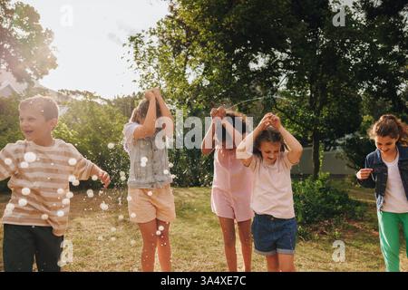 Fünf Kinder genießen spielerische Aktivitäten in einer sonnigen Umgebung im Freien, interagieren mit Wasserballons und haben Spaß, symbolisieren Freude, Gesellschaft, Stockfoto