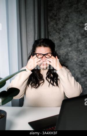 Junge Freiberufler, die von zu Hause aus arbeiten, fühlen sich müde, nachdem sie den ganzen Tag vor dem Computer gearbeitet haben. Müde Augen, Augenschmerzen. Reduzierung von Spannung und Ermüdung. Stockfoto