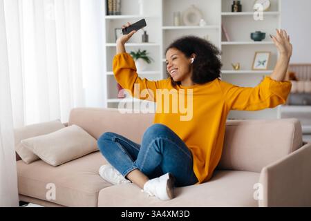 Junge Schwarze Frau, Die Schnurlose Kopfhörer Trägt Und Musik Auf Dem Smartphone Zu Hause Hört Stockfoto