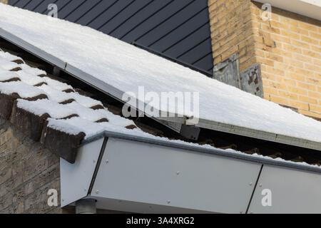 Private Sonnenkollektoren mit Schnee auf einem freistehenden Bungalow-Familienhaus auf dem Dach im Winter. Stockfoto