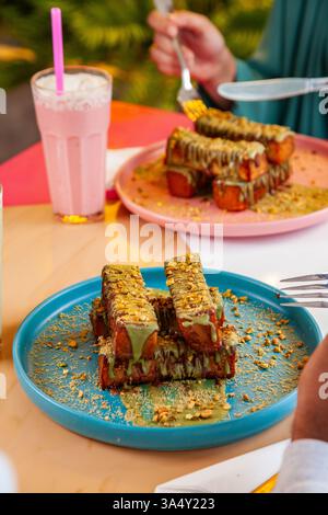 Weibliche und männliche Gäste genießen französischen Toast im Kunafa-Stil, serviert mit Milchshakes in einem schicken Café-Restaurant. Stockfoto