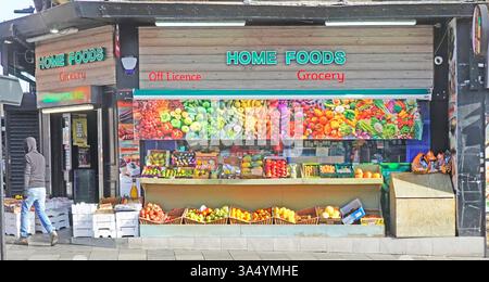 Die farbenfrohe Geschäftsfassade für Lebensmittel und Lebensmittel ohne Lizenz, die durch ein gedrucktes Banner unterstützt wird, wiederholt einige echte Lebensmittel unten im Eckladen Chelmsford Essex UK Stockfoto