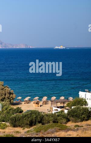 IOS, Griechenland - 8. September 2024 : Blick auf den wunderschönen Sandstrand mit Liegestühlen, Sonnenschirmen und einem Fährboot am Psathi Strand in iOS Griechenland Stockfoto