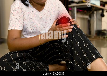 Die junge Frau sitzt auf dem Boden und legt eine kalte Kompression auf das Knie, während sie nach Schmerzen sucht. Stockfoto