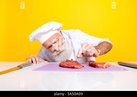 Professioneller Küchenchef, der die Zubereitung von rohem Fleisch mit konzentriertem Ausdruck in lebendiger Küche überprüft Stockfoto
