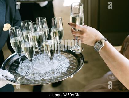 Ein Kellner präsentiert einem Gast ein Tablett mit Sektflöten bei einer eleganten Tagesveranstaltung, bei der die Feier präsentiert wird. Stockfoto