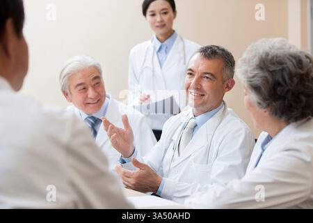 Medizinische Fachkräfte versammelten sich an einem Meeting-Tisch und diskutierten Ideen im Gesundheitswesen. Das vielfältige Team kommuniziert, arbeitet und plant selbstbewusst. Ideal für das Gesundheitswesen, medizinische Teamarbeit und professionelle Meetings. Stockfoto