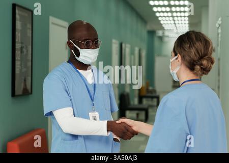 Serious Black man schüttelt einem Kollegen in einem Krankenhausflur die Hand. Das Gesundheitswesen vermittelt Teamarbeit, Professionalität und Vertrauen in eine klinische Umgebung. Stockfoto