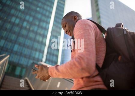 Portrait junger schwarzer Mann, der auf einer Rolltreppe in der Stadt mit Handy und Tasche steht Stockfoto