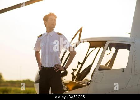 Der chinesische Hubschrauberpilot steht bei Tageslicht neben einem Hubschrauber im Freien. Ein ideales Bild in der Luft- und Raumfahrt für Schulungen, Karrieren oder Branchenmerkmale. Stockfoto