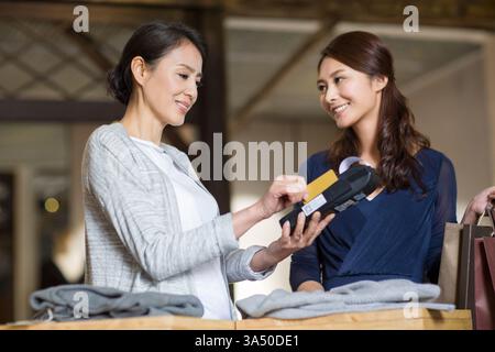 Kunde und Ladenbesitzer bezahlen per Kreditkarte in einem Bekleidungsgeschäft. In dieser Einzelhandelsszene werden moderne Zahlungsmethoden und alltägliche Einkäufe in einer Modeumgebung beleuchtet. Stockfoto