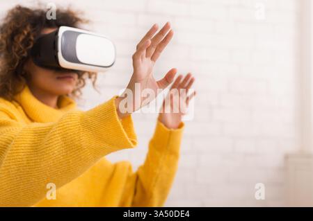 Eine Frau verwendet zu Hause ein VR-Headset, während sie eine virtuelle Umgebung mit Gesten erkundet. In der Szene werden interaktive Technologien und ein futuristischer Lebensstil zu Hause vorgestellt. Hervorragend geeignet für Kampagnen im Bereich Technik, virtuelle Realität und digitale Innovation. Stockfoto