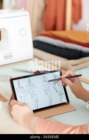 Der Modedesigner zeichnet auf einem Tablet Skizzen für eine neue Kollektion, die Design und Technologie miteinander verbindet. Hervorragend geeignet für Visuals der Modeindustrie, Designstudios und kreative professionelle Kampagnen. Stockfoto