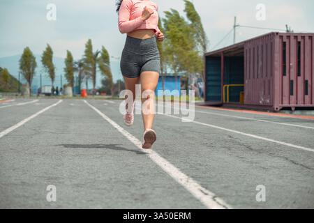 Nicht identifizierbare Sportlerin in Sportbekleidung auf einer Stadionlaufbahn an einem bewölkten Morgen. Ideal für Fitness-, Trainings- und Motivationsaufnahmen mit einer abgeschnittenen Aufnahme für Privatsphäre. Die Szene vermittelt Energie, Fokus und Wellness im Freien. Stockfoto