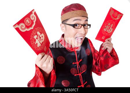 Ein überraschter chinesischer Mann in traditioneller Kleidung hält während eines festlichen Moments eine rote Tasche. Der rote Umschlag und der feierliche Ausdruck spiegeln die Traditionen des chinesischen Neujahrs und viel Glück wider. Dieses Bild ist ideal für kulturelle Feiern, Lifestyle und Feiertage. Stockfoto