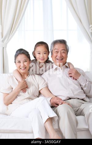 Glückliche chinesische Großeltern mit Enkelin, die drinnen als ein generationenübergreifender Familienmoment gefangen wurden. Eine herzliche, liebevolle Szene, in der Familienbande und Zusammengehörigkeit hervorgehoben werden. Geeignet für Familienleben, Altenpflege und häusliches Leben. Stockfoto