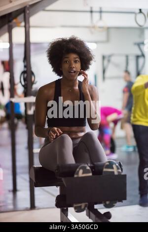 Jugendliche Afroamerikanerin, die Sit-ups in einem Fitnessstudio macht. Das Bild zeigt das Bauchtraining und den Kraftaufbau im Fitnessstudio. Ideal für Fitness-Aktionen, Cardio-Workouts und Kampagnen für gesunden Lebensstil. Stockfoto