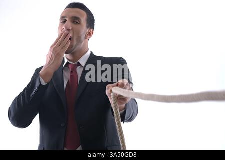 Geschäftsmann aus dem Nahen Osten zieht ein Seil in einem Studio auf weißem Hintergrund. Ein starkes Konzeptbild für Aufwand, Druck und Herausforderungen am Arbeitsplatz. Nützlich für Geschäfts-, Führungs- und Karrierethemen. Stockfoto