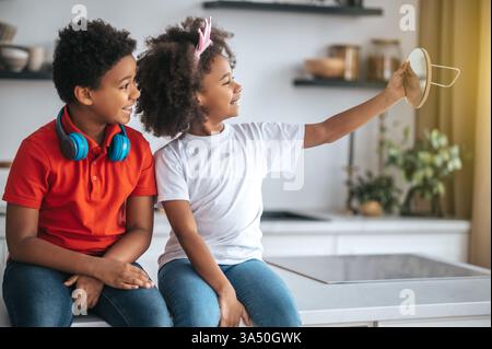 Zwei Geschwister genießen die Zeit zu Hause, lächeln und fühlen sich fröhlich. Dieses warme Lifestyle-Bild eignet sich hervorragend für Familien-, Heim- und Wohlfühlthemen. Stockfoto