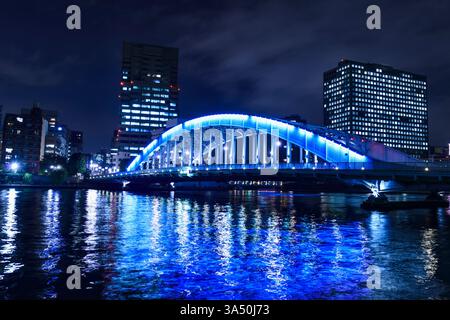 Nächtlicher Blick auf Tokio mit dem Sumida-Fluss und der Eitai-Brücke, beleuchtet vor einer Skyline von Hochhäusern. Ideal für Reisen, nächtliche Stadtfotografie und Architekturmerkmale. Ideal für die Abdeckung des Stadtlebens von Tokio und der urbanen Landschaften mit Reflexionen auf dem Wasser. Stockfoto