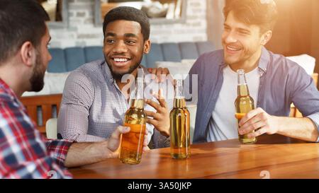 Drei Freunde in einem Pub teilen sich einen fröhlichen Moment, sprechen und toasten mit Getränken. Diese offene Lifestyle-Szene ist perfekt für Gastfreundschaft, Nachtleben und Freundschaftskampagnen. Ideal für die Vermarktung von Bars, Restaurants und gesellschaftlichen Anlässen. Stockfoto