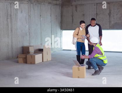 Ein vielseitiges Paar mit einem Tablet berät einen kaukasischen Ingenieur, der auf einer Baustelle Pläne für die Hausplanung zeigt. Themen für Wohnbau, Architektur und Zusammenarbeit, die sich für Immobilien- und Bauprojekte eignen. Stockfoto
