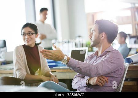 Chinesische weibliche und kaukaukausische männliche Büroangestellte, die im Büro auf Stühlen sitzen Stockfoto