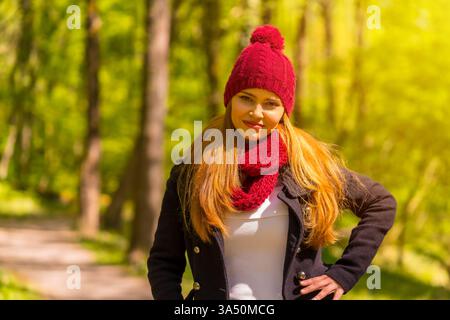 Die junge Latina in einer schwarzen Jacke, einem roten Wollmütze und einem Schal genießt einen Herbsttag im Park. Ideal für Lifestyle, Outdoor-Mode und saisonale Kampagnen. Stockfoto