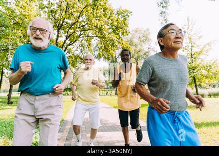 Verschiedene Gruppe von Senioren, die in einem sonnigen Park trainieren und joggen. Ein positives Lifestyle-Bild, das anmutiges Altern, Fitness und Kameradschaft veranschaulicht. Stockfoto