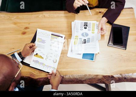 Hochwinkelansicht von zwei Anwälten an einem Tisch, die Finanzdokumente und Diagramme während eines Geschäftstreffens prüfen. Perfekt für Unternehmensfinanzen, juristische Teamarbeit und professionelle Zusammenarbeit. Stockfoto