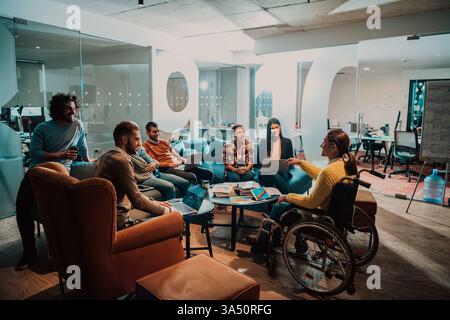Eine Geschäftsfrau im Rollstuhl nimmt an einem Geschäftstreffen mit Kollegen in einem modernen Büro Teil. Das vielfältige Team arbeitet an Online-Geschäftsideen zusammen und hebt Inklusion und Teamarbeit in einem modernen Arbeitsbereich hervor. Stockfoto
