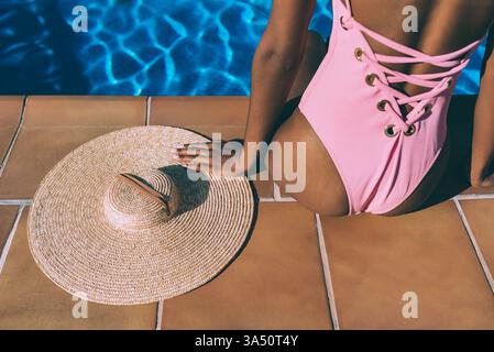 Poolszene mit einer schwarzen Frau mit Strohhut. Dieses Freizeitbild vermittelt Urlaubs- und Resortatmosphäre mit Sonne und Wasser. Ideal für Reisen, Lifestyle und Entspannung. Stockfoto