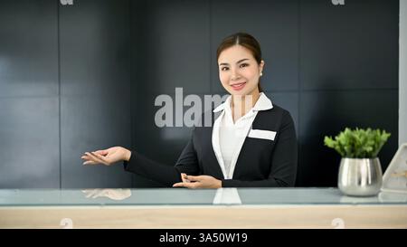 Freundliche, tausendjährige asiatische Rezeptionisten in ordentlicher Uniform begrüßen die Gäste an der Rezeption in einer modernen Hotellobby. Der Begrüßungsservice funktioniert gut für Marketing im Gastgewerbe, Check-in-Szenen und Personal an der Rezeption. Ein geschliffenes Image, das Professionalität und ansprechenden Service vermittelt. Stockfoto