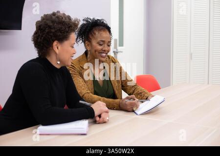Zwei professionelle Frauen, die ein Meeting drinnen in einer Geschäftsumgebung veranstalten. Die Szene vermittelt Teamarbeit und Führungsqualitäten für Unternehmenskommunikation und Frauen am Arbeitsplatz. Ideal für Marketingmaterialien zu Meetings, Zusammenarbeit und weiblichen Geschäftsleuten. Stockfoto