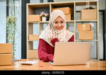 Eine asiatische Unternehmerin, die Hijab trägt, verwendet ein Smartphone, um mit einem Kunden in Verbindung zu treten. Diese moderne Online-Geschäftsszene für KMU legt den Schwerpunkt auf digitale Kommunikation und die Stärkung von Frauen. Nützlich für Branding im Bereich Online-Handel, Unternehmertum und mobile Dienste. Stockfoto
