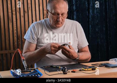 Reife Männer tragen ein Denim-Shirt, das in seinem Heimbüro mit elektronischen Komponenten arbeitet Stockfoto