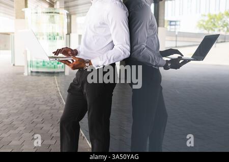 Seitenansicht eines gesichtslosen afroamerikanischen Unternehmers, der auf einem Laptop neben einem Bürogebäude der Stadt tippt. Die formelle Kleidung und die urbane Umgebung vermitteln eine moderne, professionelle Geschäftsszene. Ideal für Themen wie Unternehmergeist, Arbeitsumgebungen in der Innenstadt und Aktivitäten an entfernten Standorten. Stockfoto