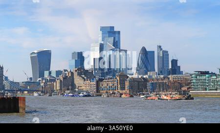 Die Skyline der City of London erhebt sich hinter viktorianischen Lagerhäusern von Wapping und der Themse. 2025. Zeigt traditionelle Segelkähne und den Flussverkehr. Stockfoto