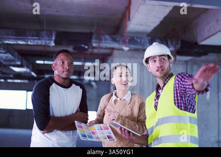 Architekt demonstriert einem vielseitigen Paar auf einer Baustelle die Pläne für die Hausgestaltung und führt sie mit einem Tablet an. Dieses Bild passt zu Inhalten über Architekturplanung, Wohnplanung und Bauprojekte. Stockfoto