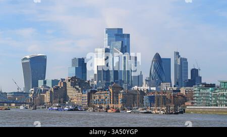 Die Skyline der City of London erhebt sich hinter viktorianischen Lagerhäusern von Wapping und der Themse. 2025. Zeigt traditionelle Segelkähne und den Flussverkehr. Stockfoto