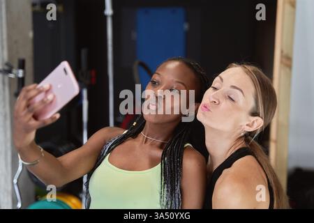 Zwei Fitnessfreunde machen ein fröhliches Selfie mit einem Handy nach einem Workout im Fitnessstudio. Dieses Lifestyle-Bild passt zu Fitness, Gesundheit und Social-Media-Inhalten, die Freundschaft feiern. Helle, energiegeladene Stimmung unterstreicht Motivation und Kameradschaft. Stockfoto