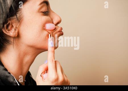 Schönheitsbehandlungen zu Hause. In einem Haarreif, der ihr Haar hält, gibt sich ein Mädchen eine Gesichtsmassage mit einem Gouachestein. Ein Gesichtsmassageroller in A Stockfoto