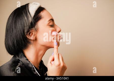In einem Haarreif, der ihr Haar hält, gibt sich ein Mädchen eine Gesichtsmassage mit einem Gouachestein. Eine Gesichtsmassage in den Händen einer Frau. Anti-Aging Stockfoto