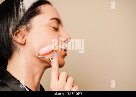 Anti-Aging-Hautmassage, Nahaufnahme. Schönheitsbehandlungen zu Hause. In einem Haarreif, der ihr Haar hält, gibt sich ein Mädchen eine Gesichtsmassage mit Gouache Stockfoto