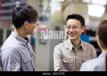 Lächelnde chinesische Ingenieure, die sich in der Fabrik anschauen Stockfoto