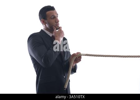 Nachdenklicher Geschäftsmann aus dem Nahen Osten zieht ein Seil in einem Studio auf weißem Hintergrund. Dieses Konzept vermittelt Anstrengungen, Stress und Herausforderungen des Unternehmens. Stockfoto