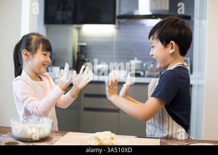 Chinesische Geschwister spielen mit Mehl in einer Küche. Ein fröhlicher Moment, der Familienleben, Kochen und Zusammensein feiert. Stockfoto
